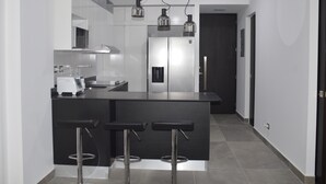 A modern kitchen with a central island, bar stools, a refrigerator, and a staircase.