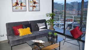 A modern living room with a grey sofa, red and yellow cushions, a black chair, and abstract art on the wall.