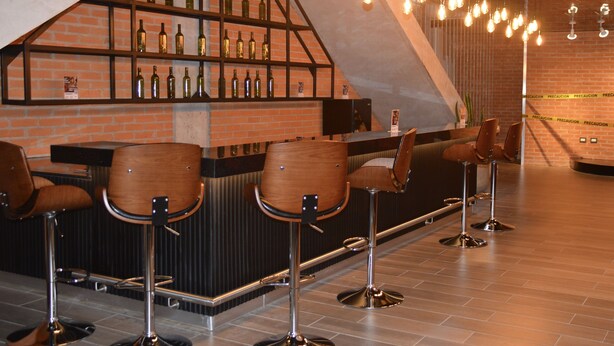 A bar area with a brick wall, shelves with bottles, and hanging light bulbs.