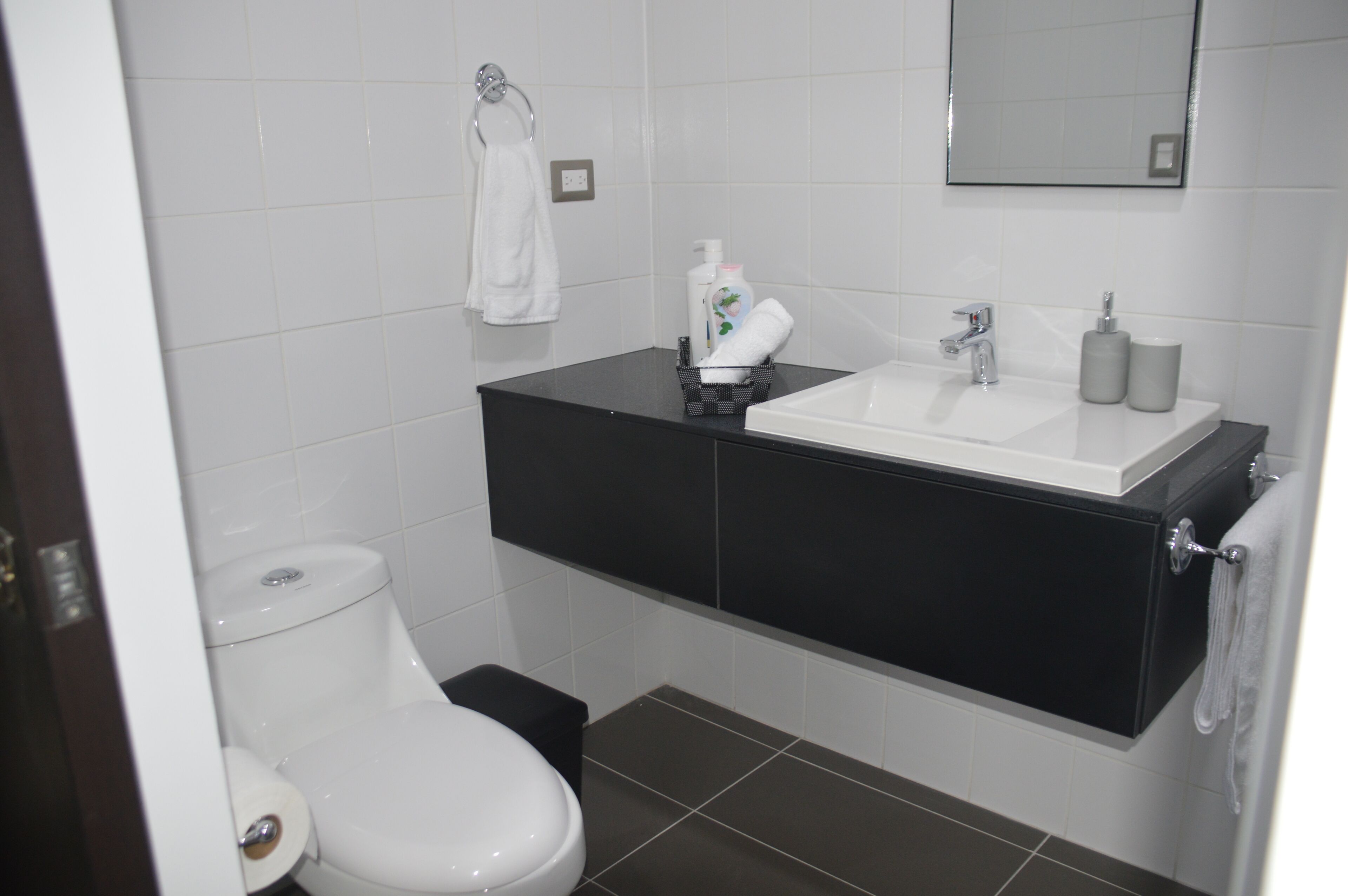 Un baño con inodoro blanco, lavamanos negro y espejo sobre él.
