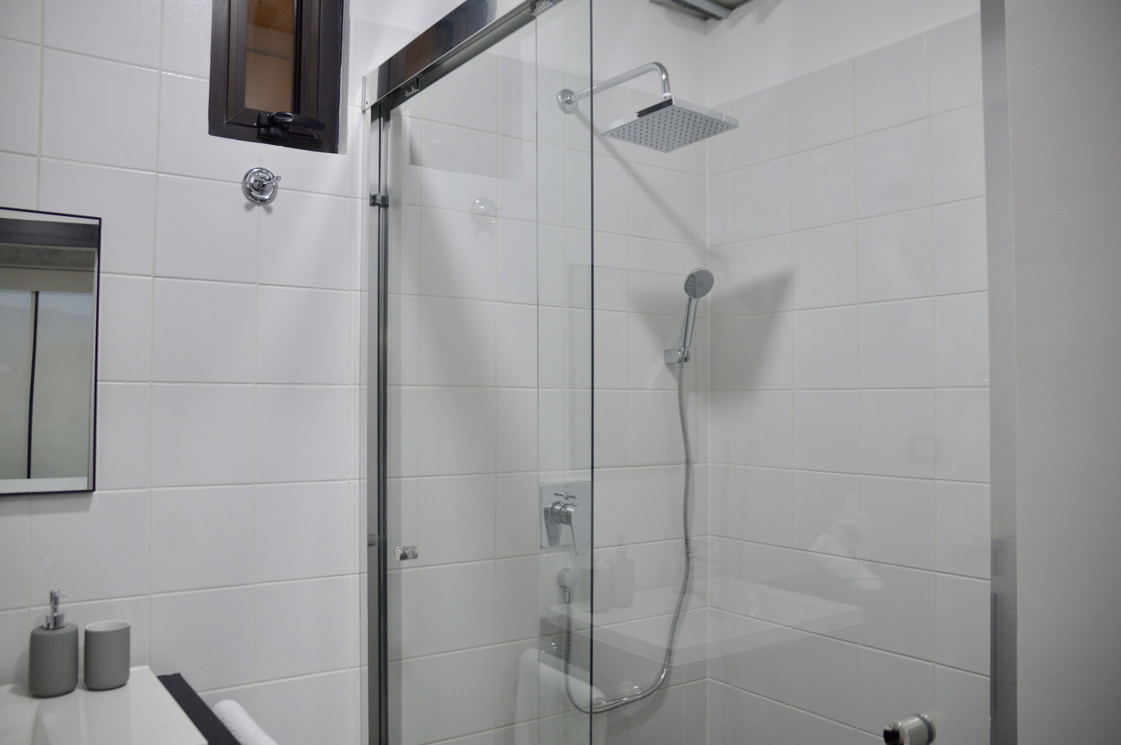 Ein modernes Badezimmer mit weißen Fliesen, einer Glaskabine für die Dusche, einer Toilette und einem Waschbecken mit zwei zylindrischen Behältern.
