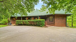 Een houten lodge met een groen dak, een overdekte veranda en een verzorgde haag ervoor.