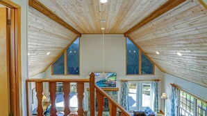 A spacious room with a high ceiling and wooden beams, a large window, and a staircase leading to an upper level. - Luxury Mountaintop Views with Hot Tub - 1 min to town (Hiawassee)