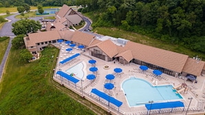An aerial view of a resort with multiple swimming pools, lounge areas, and a large building with a unique roof design.