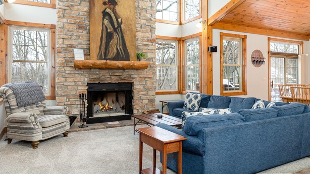 A cozy living room with a stone fireplace, a blue sofa, a striped armchair, and a wooden table.
