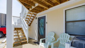 Eine überdachte Veranda mit einer Holztreppe, zwei weißen Kunststoff-Adirondack-Stühlen und einem in der Nähe geparkten roten Fahrzeug.