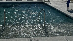 Ein Schwimmbecken mit einem Schild für eine Wassertiefe von 15 Zentimetern, Metallstühlen und einem weißen Zaun.