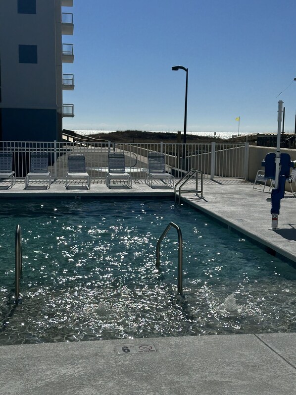 Una piscina con un cartel que indica una profundidad de 15 centímetros, sillas de metal y una cerca blanca.