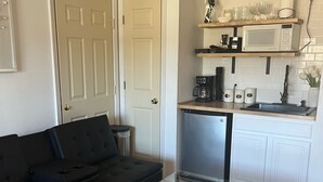 A compact living space with a glass-top table, a black sofa, a kitchen area with a microwave, and a dishwasher. - Branson, Stone Bridge Resort Studio (Reeds Spring)