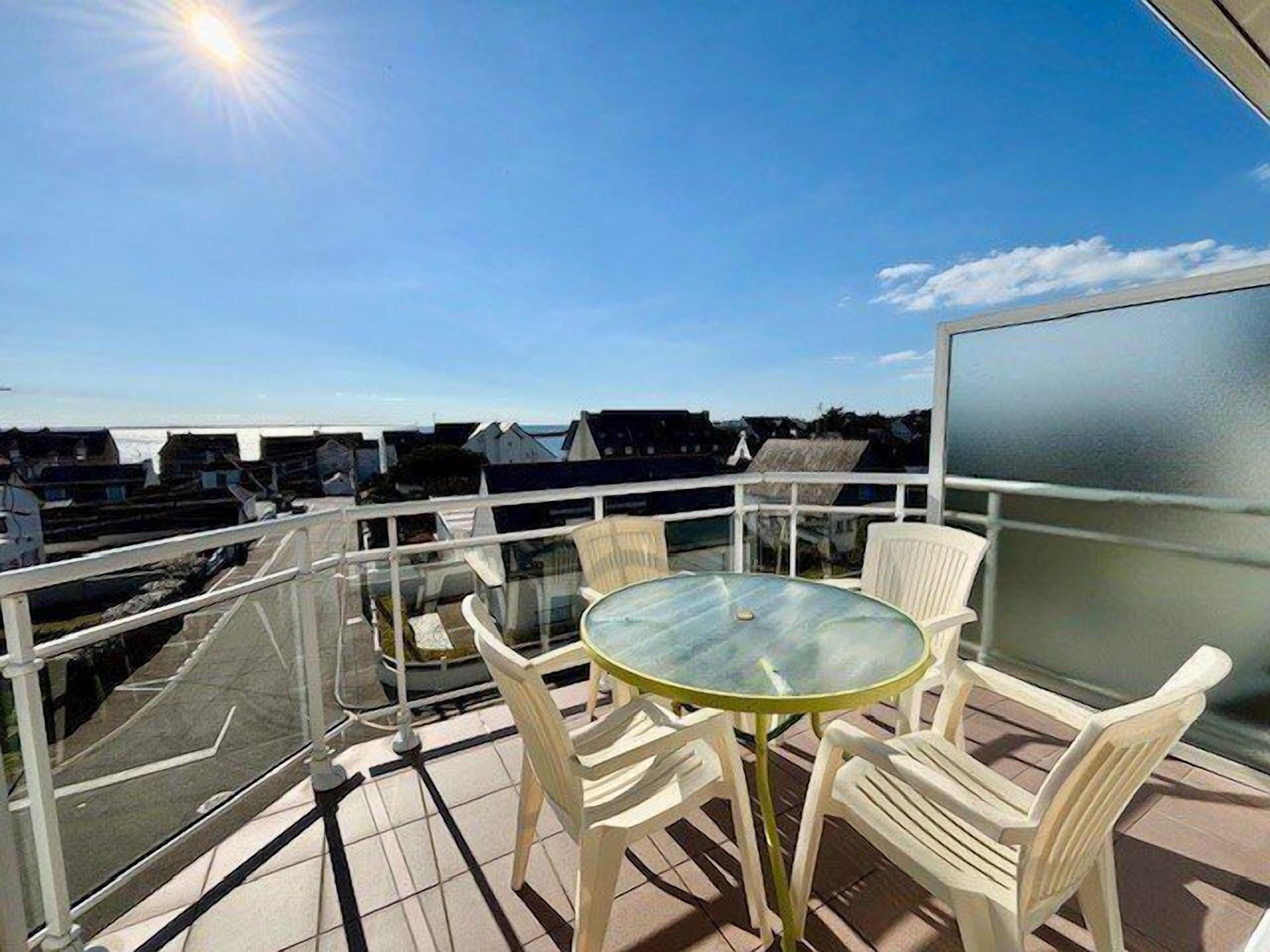 A balcony with a glass table and chairs, offering a view of the surrounding buildings.