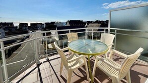Een balkon met een glazen tafel en stoelen, met uitzicht op de omliggende gebouwen.