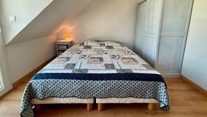 Een kleine, gezellige slaapkamer met een schuine kap, een gewatteerde sprei, een nachtkastje met lamp en een kledingkast.