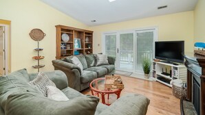 A living room with two sofas, a glass coffee table, a TV, and a bookshelf. - Family Entertainment Beach House, Hot tub, Nature Park, Fire pit, Pizza Oven (Emerald Isle)
