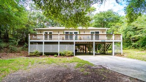 A two-story house with a covered porch and a deck, surrounded by trees. - Family Entertainment Beach House, Hot tub, Nature Park, Fire pit, Pizza Oven (Emerald Isle)