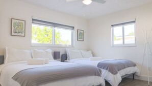 A bedroom with two beds, large windows, and a ceiling fan.