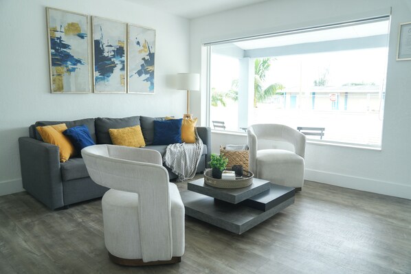 A modern living room with a grey sofa, white armchairs, and a coffee table with decorative items.