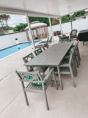 Um pátio externo com piscina, espreguiçadeiras e uma mesa de jantar.