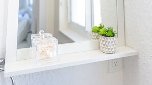 A bathroom with a white vanity, a mirror, and a shelf with a toothbrush holder and a small potted plant.