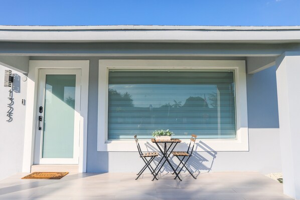 A modern exterior with a sliding glass door, a small table with chairs, and a potted plant.