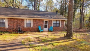 A single-story brick house with a front porch, two blue Adirondack chairs, and a visible door. - Entire Townhome Your GameDay Getaway 5Miles away from Sanford Stadium (Athens)