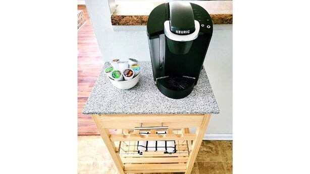 A Keurig coffee maker on a granite countertop with a coffee pod holder and a wooden cart with a metal rack underneath. - Entire Townhome Your GameDay Getaway 5Miles away from Sanford Stadium (Athens)
