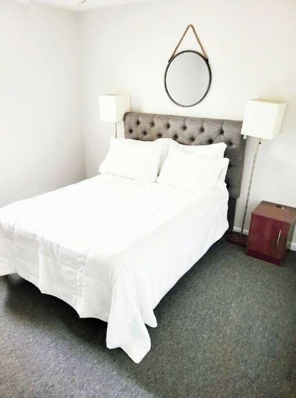 A neatly made bed with white linens, a tufted headboard, and two bedside lamps.
