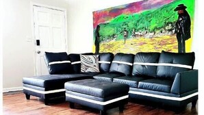 A living room with a black leather sectional sofa, a matching ottoman, and a colorful abstract painting on the wall. - Entire Townhome Your GameDay Getaway 5Miles away from Sanford Stadium (Athens)