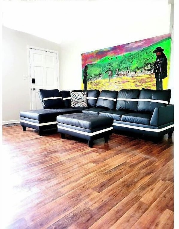 Un salon avec un canapé d’angle en cuir noir, un pouf assorti et un tableau abstrait aux couleurs vives accroché au mur.
