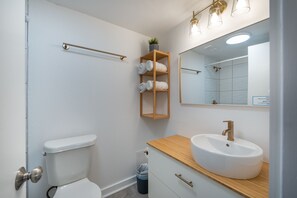 A modern bathroom with a white toilet, wooden vanity, and a large mirror. - NEW - Spacious Studio close to Theme Parks (Orlando)