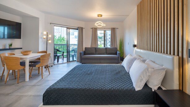 A modern hotel room with a large bed, a sofa, a dining table with chairs, and a balcony with a view of the city. - NEW - Spacious Studio close to Theme Parks (Orlando)