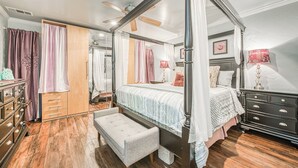 A four-poster canopy bed with a bench, wooden floor, and a wardrobe with multiple drawers.
