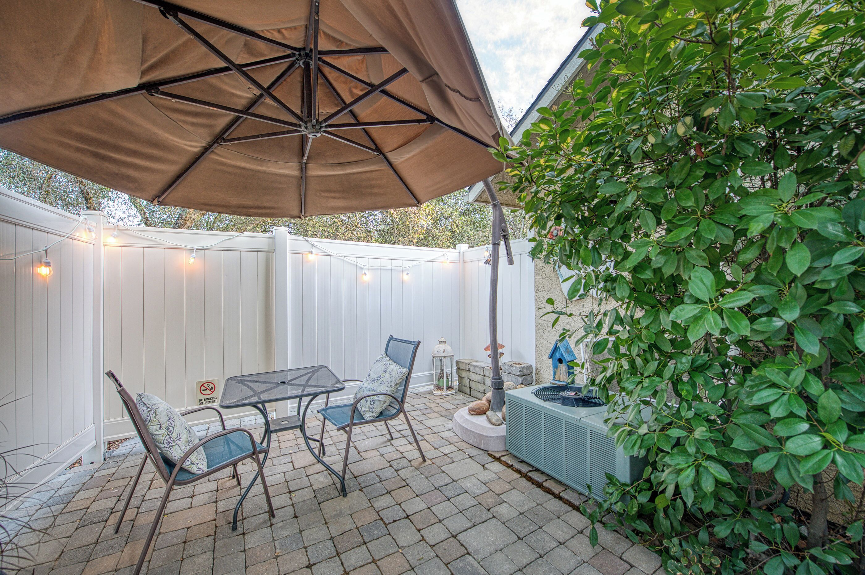 Une terrasse avec une table et des chaises, un parasol suspendu et une clôture blanche.