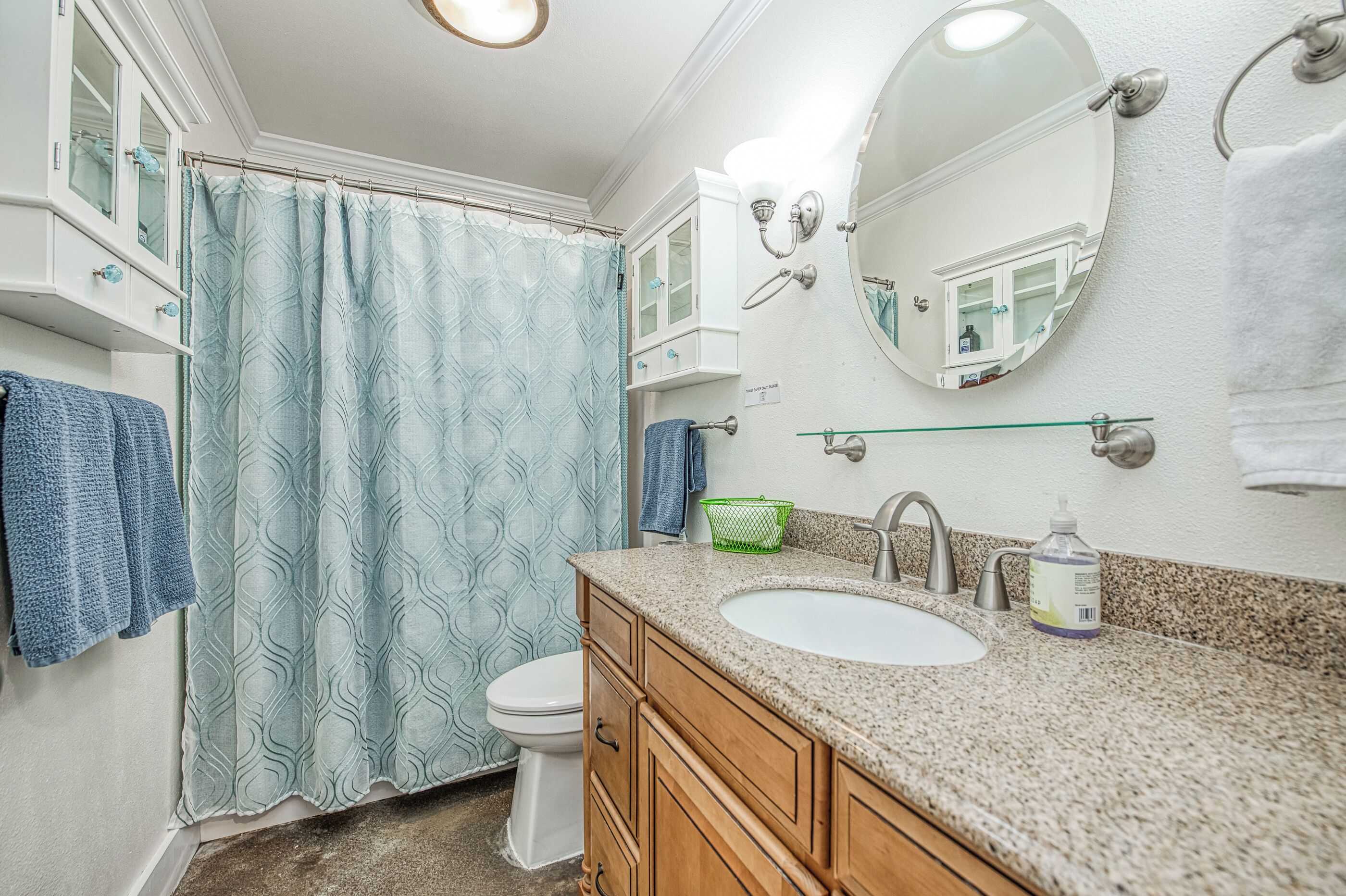 Une salle de bain avec des toilettes blanches, un lavabo doté d’un plan de travail en granit, un miroir et un rideau de douche.