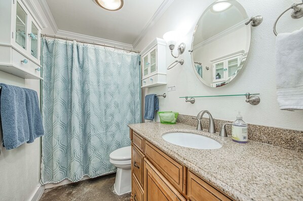 Un baño con inodoro blanco, un lavabo con encimera de granito, un espejo y cortina de ducha.