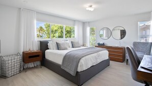 Een moderne slaapkamer met een groot bed, nachtkastjes, een bureau en een stoel.
