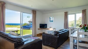 A modern living room with a sofa, a TV, and a dining area with a table and chairs. - Harbour Lodge (Port Isaac)