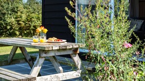 A wooden picnic table with a plate of food, a glass of orange juice, and a vase of flowers. - Harbour Lodge (Port Isaac)