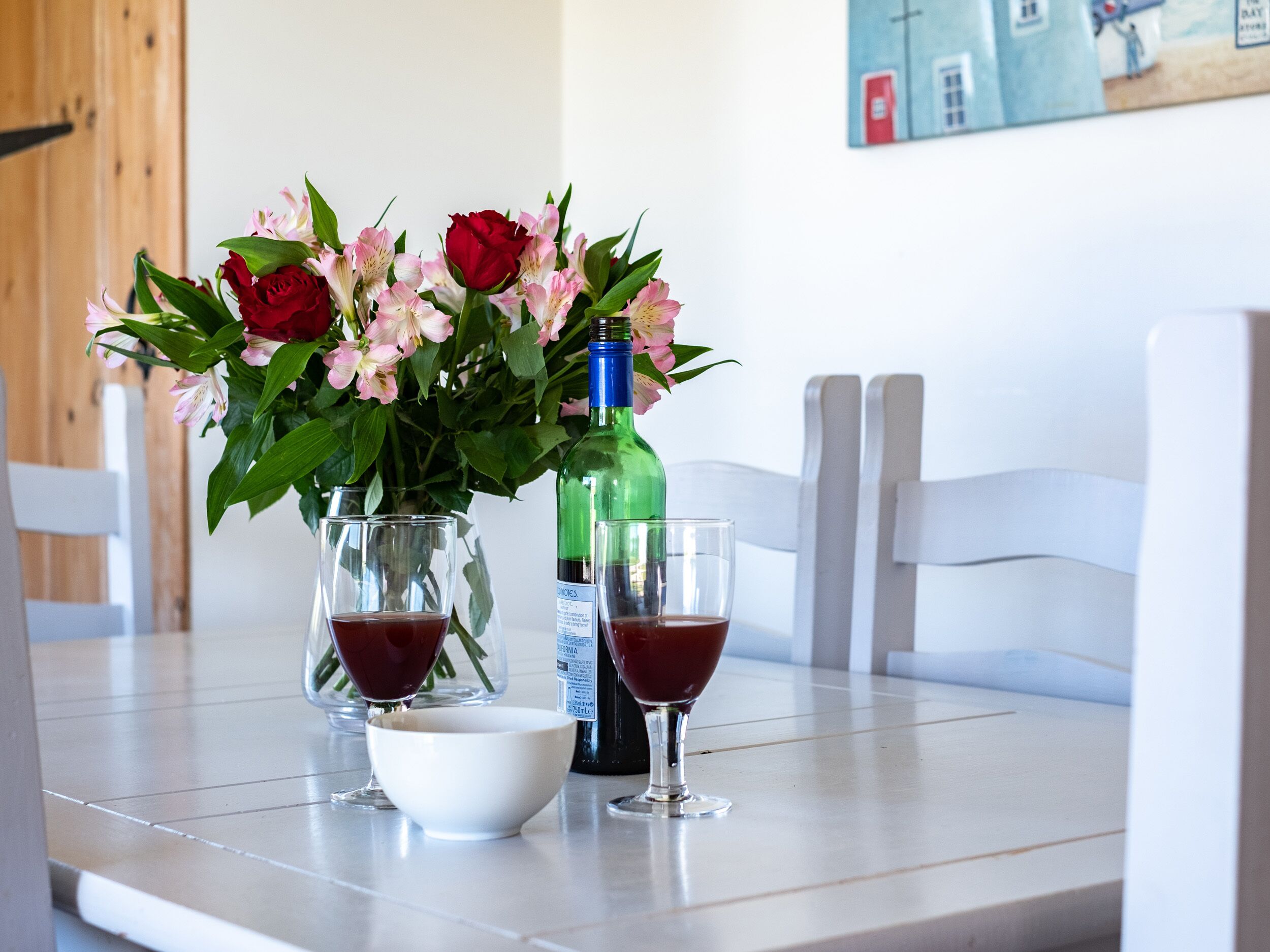 Ein Tisch mit einer Blumenvase, einer Flasche und zwei Gläsern rote Flüssigkeit.