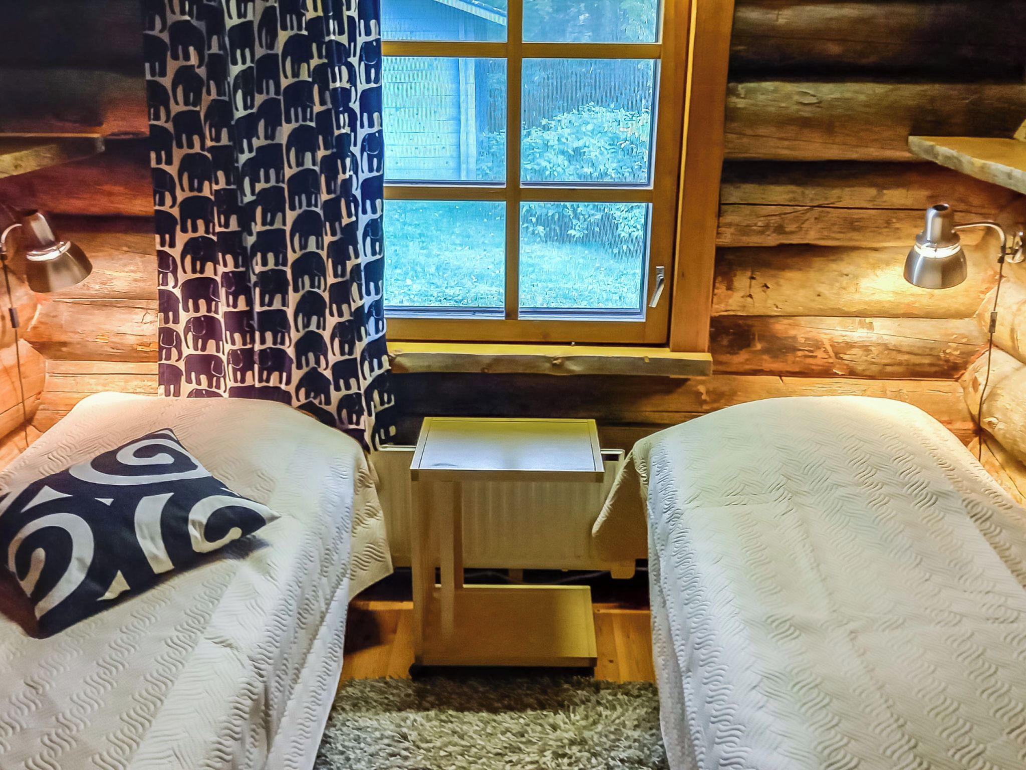 Una cabaña con dos camas, un ventanal con vistas a árboles y un escritorio pequeño.