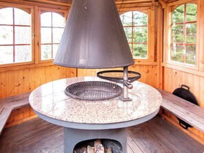 Ein Zimmer mit Holzboden, einem runden Steintisch, einem Metallgitter und einem Kamin.