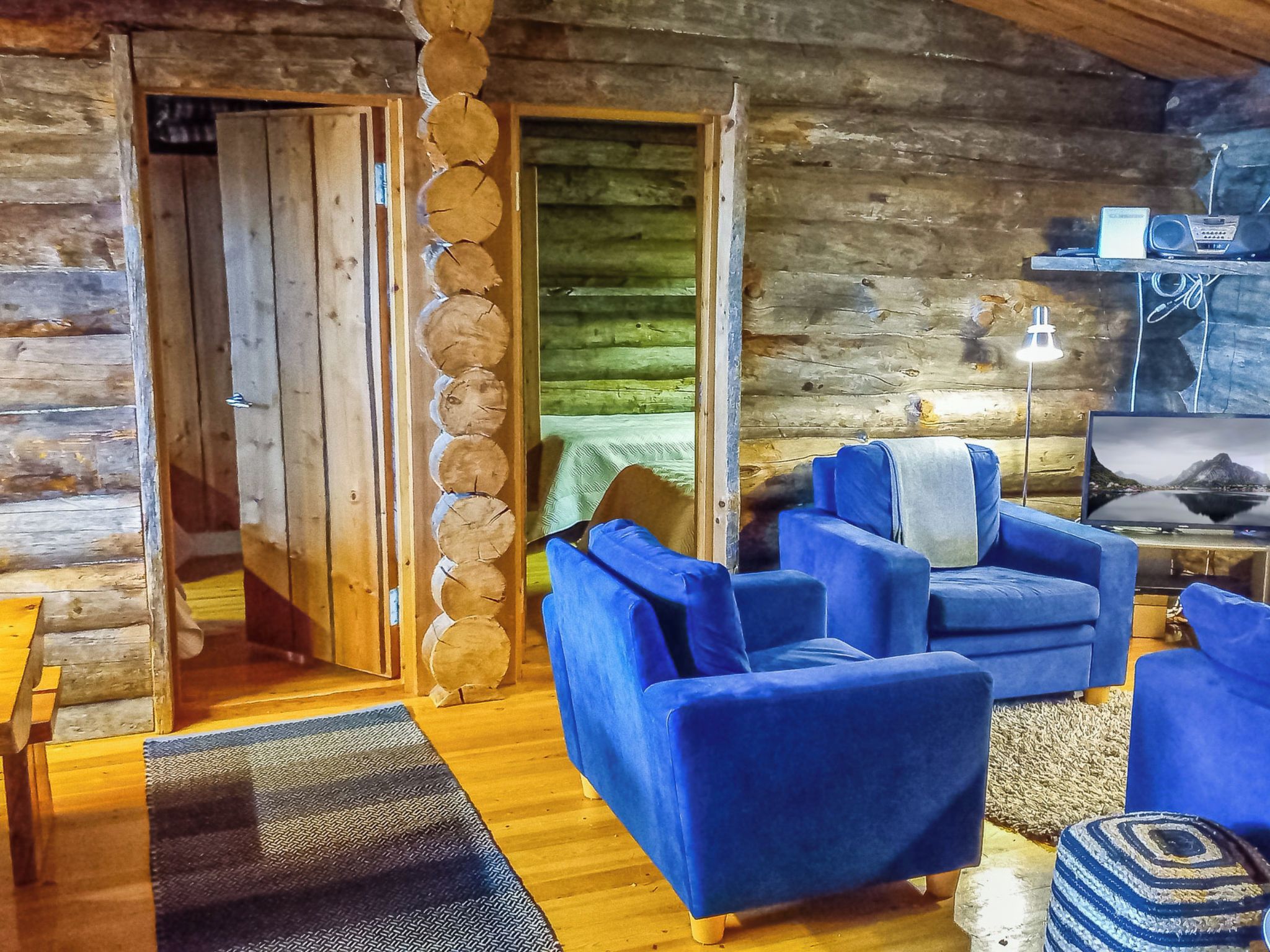A log cabin interior with a wooden floor, blue sofas, a television, and a lamp.