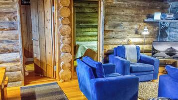A log cabin interior with a wooden floor, blue sofas, a television, and a lamp.