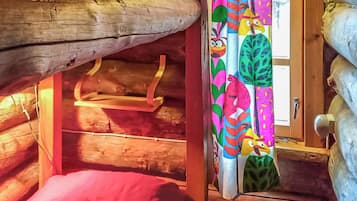 Interior acogedor de una cabaña con techo de madera, un pequeño banco y una cortina colorida con personajes de dibujos animados.
