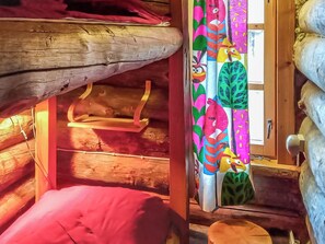 A cozy cabin interior with a wooden ceiling, a small bench, and a colorful curtain with cartoon characters.