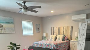 Una sala moderna con un sofá oscuro, almohadones coloridos, un tapete estampado y un ventilador de techo.