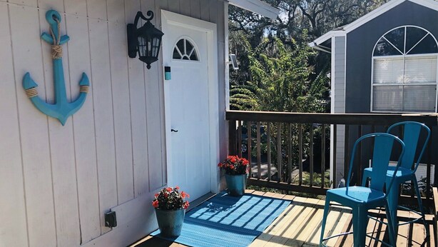 Una terraza de madera con un tapete azul, dos plantas en macetas y dos sillas azules.