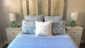 Una cama con colcha azul, dos mesitas de noche con lámparas y una alfombra estampada.