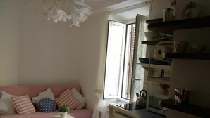 Ein gemütliches Wohnzimmer mit einem rosafarbenen Sofa, einem kleinen weißen Tisch mit einer Pflanze und einer Küchenzeile mit Spüle und Herd.