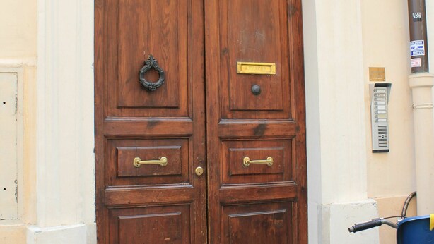 Eine doppelte Holztür mit Messingklinke und Messingschild, eingelassen in ein Gebäude mit weißer Fassade und einem Schild mit der Aufschrift '33'.