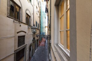 A narrow alleyway between buildings with a street lamp, a small gate, and a window with a curtain.